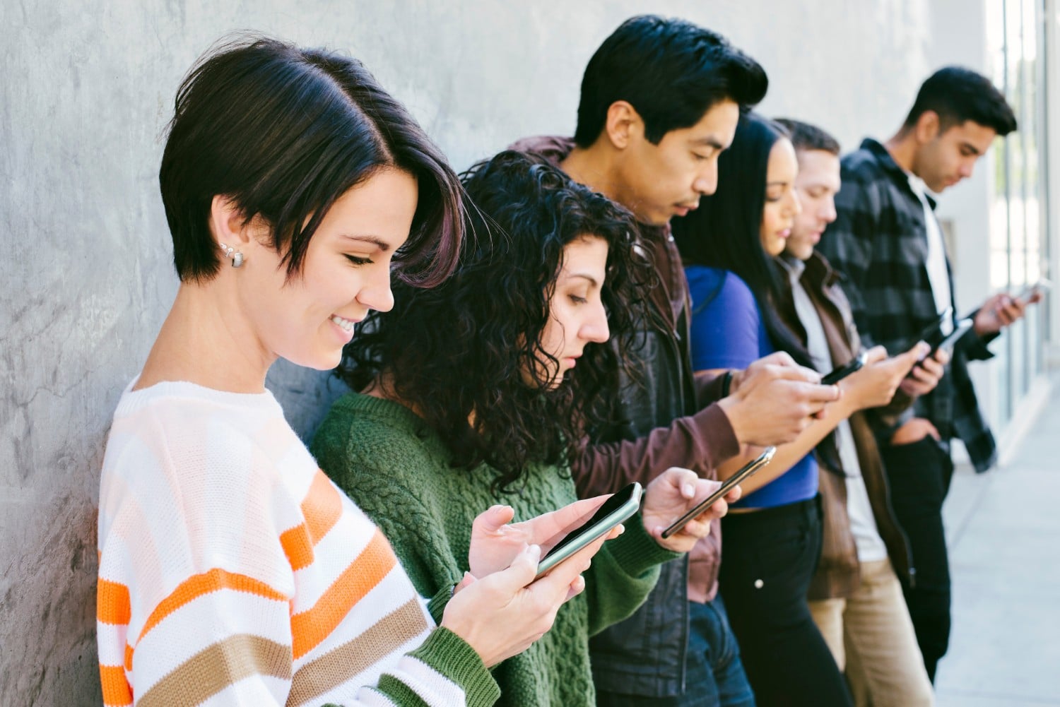 a group of people leaning against a wall looking at their phones