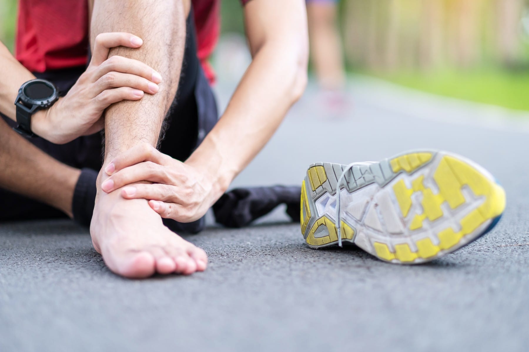 man sitting on a path with his shoe off holding his achilles tendon