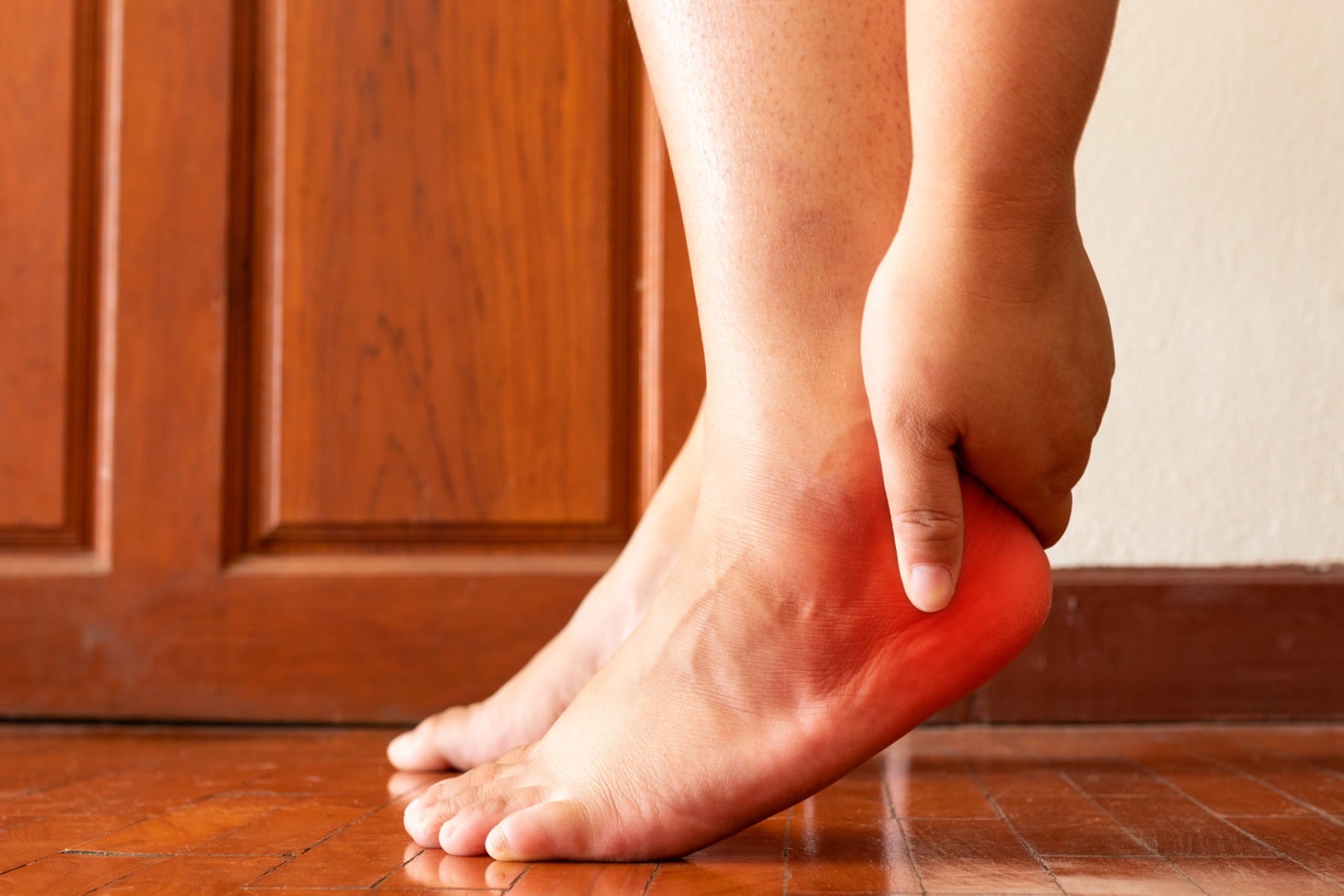 person in their home reaching down and holding their heel in pain